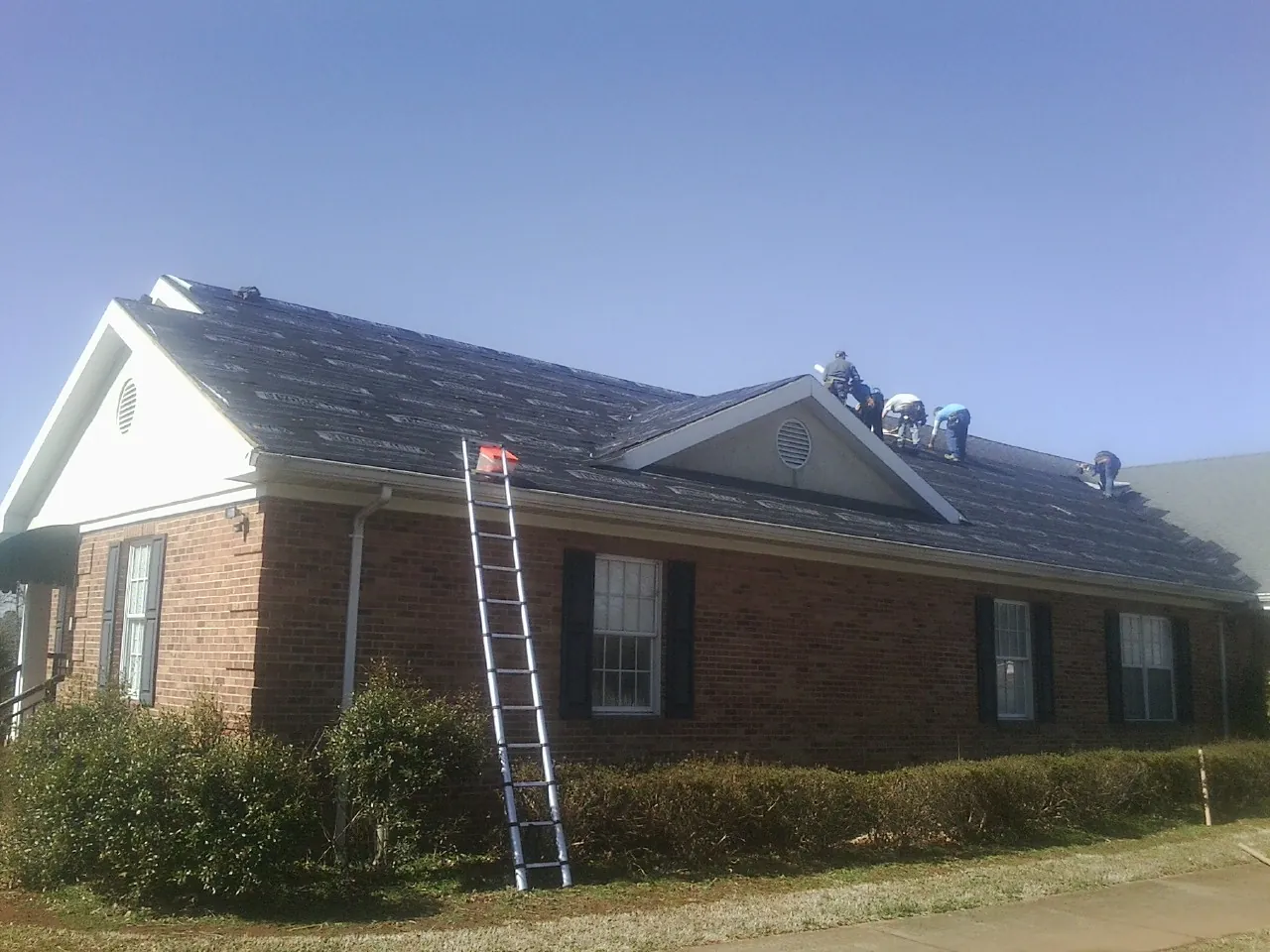 Crew tearing shingles off a brick ranch roof with a ladder set — Metal Roof Repair work by our crew in Arlington